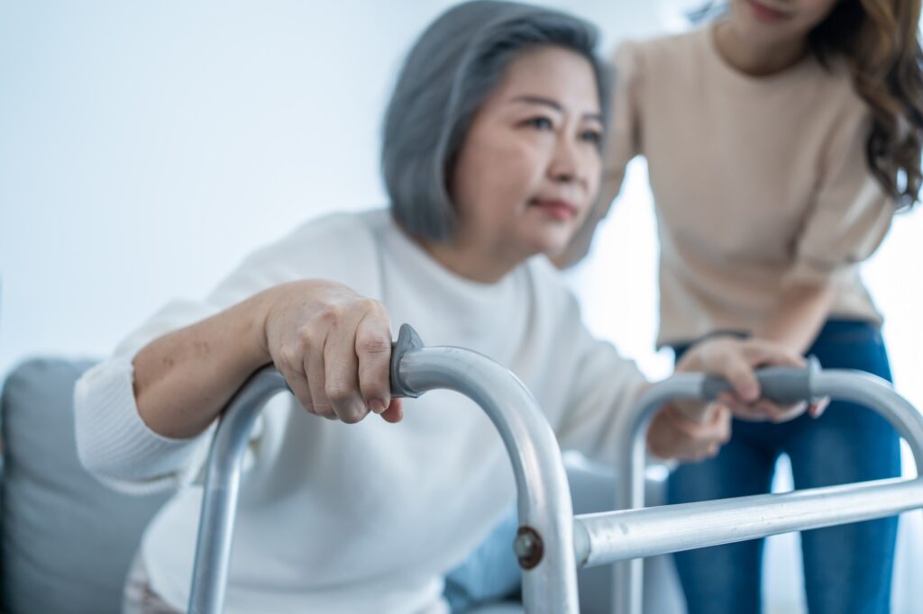 Asian young daughter support old disabled woman walk with walker at home.