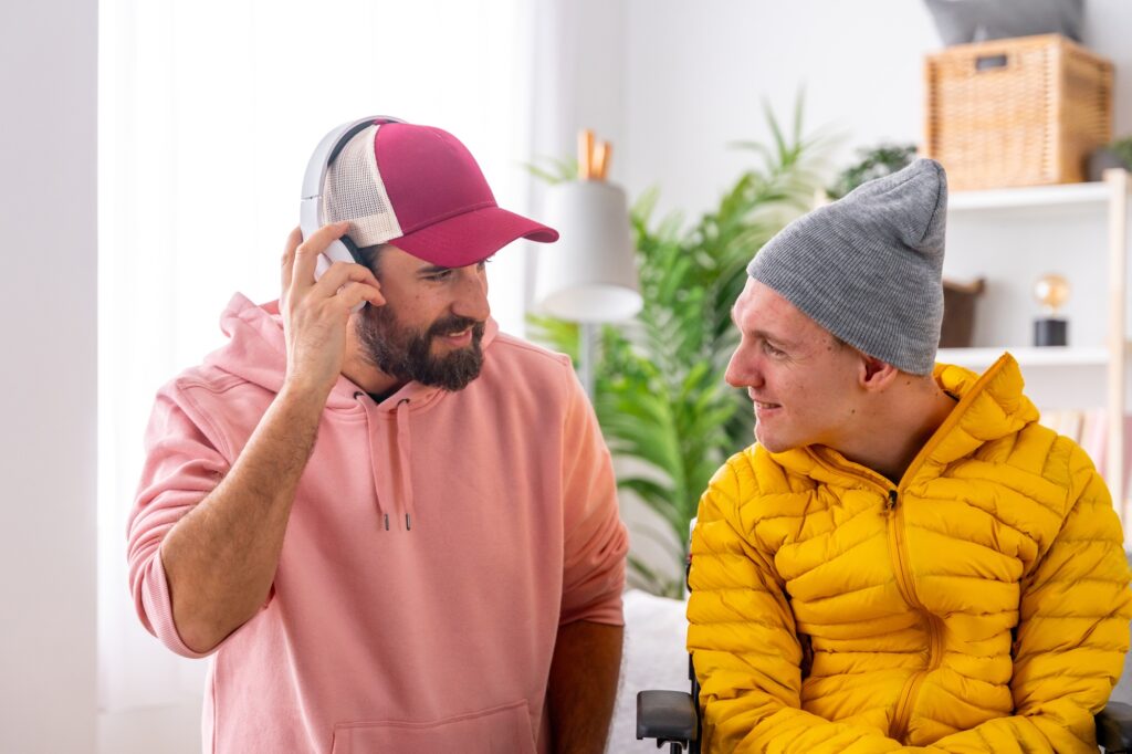 Man listening to music next to a disabled friend indoors